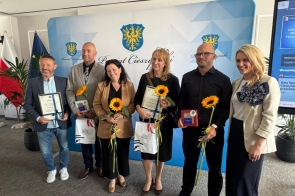 Grupa wyróżnionych osób pozuje do zdjęcia podczas gali sportu, trzymając dyplomy, statuetki i słoneczniki. 