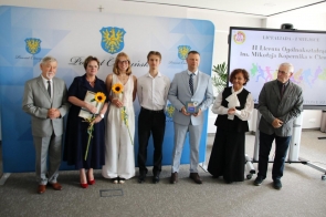 Grupa wyróżnionych osób pozuje do zdjęcia podczas gali sportu, trzymając dyplomy, statuetki i słoneczniki. 