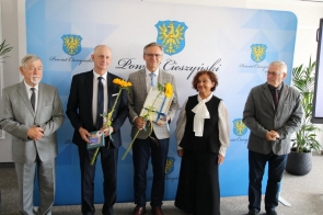 Grupa wyróżnionych osób pozuje do zdjęcia podczas gali sportu, trzymając dyplomy, statuetki i słoneczniki. 