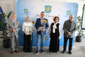 Grupa wyróżnionych osób pozuje do zdjęcia podczas gali sportu, trzymając dyplomy, statuetki i słoneczniki. 