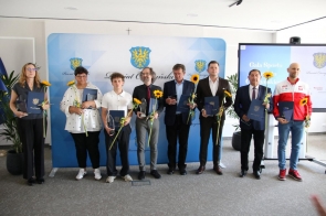 Grupa wyróżnionych osób pozuje do zdjęcia podczas gali sportu, trzymając dyplomy, statuetki i słoneczniki. 