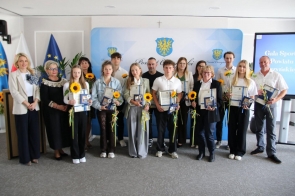 Grupa wyróżnionych osób pozuje do zdjęcia podczas gali sportu, trzymając dyplomy, statuetki i słoneczniki. 