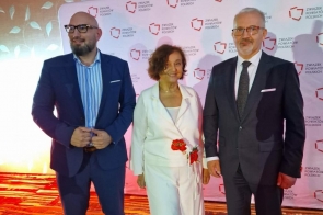 Trzy osoby pozują do zdjęcia na tle ścianki z napisem „Związek Powiatów Polskich”. Wszyscy są ubrani elegancko, a sala jest oświetlona czerwonym światłem.