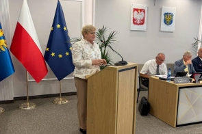 Małgorzata Pępek Poseł na Sejm RP stoi przy mównicy i przemawia do mikrofonu w sali obrad. W tle widać flagi, godło Polski, herb Powiatu Cieszyńskiego oraz osoby siedzące przy stole prezydialnym.