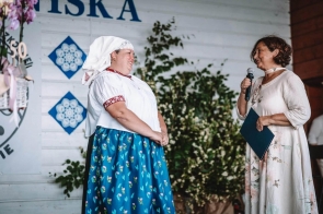 Na zdjęciu widać dwie kobiety podczas. Ewa Macoszek-Dragon Dyrektor Ogniska Pracy Pozaszkolnej w Koniakowie ubrana jest w tradycyjny strój regionalny z białą chustą i niebieską spódnicą w kwiaty, a Janina Żagan Starosta Cieszyński stoi obok i trzyma mikrofon.