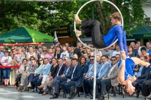 Dwoje artystów w niebieskich strojach wykonuje akrobacje na białej obręczy przed liczną publicznością.