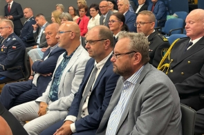 Publiczność siedzi w sali konferencyjnej. Wśród osób widoczni są przedstawiciele służb w mundurach oraz uczestnicy w strojach formalnych.