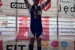 Szymon Machej stoi na pierwszym miejscu podium podczas zawodów Olimpiad Specjalnych, unosi ręce w geście zwycięstwa i ma na szyi zdobyte medale.