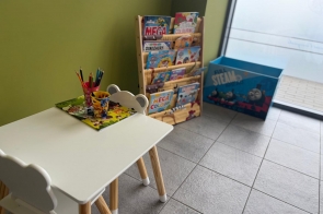 Kącik dziecięcy przy oknie – biały stolik i krzesełko, kredki, kolorowanki, stojak z książeczkami oraz pojemnik na zabawki.