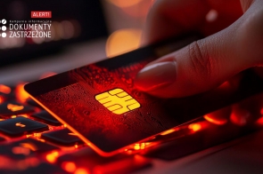 Ciemne tło z intensywnym czerwonym oświetleniem podkreśla ostrzegawczy charakter grafiki. W centrum dłoń trzymająca kartę płatniczą, której mikroprocesor odbija światło, nadając jej nowoczesny wygląd. Klawiatura laptopa w tle jest podświetlona na czerwono, co nawiązuje do cyberzagrożeń. W górnym lewym rogu biały tekst kampanii ostrzegawczej o dokumentach zastrzeżonych z napisem "ALERT!".
