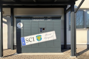 Urzędomat ustawiony przy budynku. Na urządzeniu widoczne są oznaczenia Powiatu Cieszyńskiego, logo Śląska Cieszyńskiego oraz grafika tablicy rejestracyjnej.
