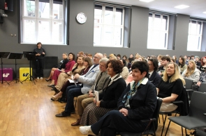 Zaproszeni goście oraz uczniowie siedzą na krzesłach w sali konferencyjnej. Goście ubrani w eleganckie stroje.