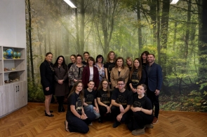 Grupa osób stoi i klęczy do wspólnego zdjęcia w pomieszczeniu z leśną grafiką na ścianie, obok widać regał z globusami.