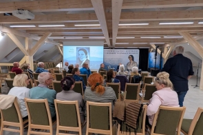 Uczestnicy siedzą na krzesłach w sali Centrum Eduukacyjno-Kulturalnego „U Kossaków” podczas spotkania. Na końcu sali widoczny jest ekran z prezentacją oraz baner wydarzenia.
