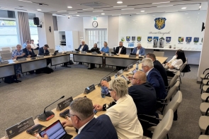 Radni podczas sesji w sali sesyjnej Starostwa Powiatowego. Na stołach widoczne są tablety, dokumenty oraz tabliczki z nazwiskami, a w tle znajduje się herb Powiatu.