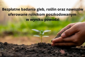 Na zdjęciu znajduje się młoda roślina wyrastająca z ziemi. Dłoń ludzka delikatnie trzyma ziemię wokół tej rośliny. W tle są rozmyte, naturalne kolory zieleni, co charakterystyczne dla gospodarstw rolnych lub wiejskich. Na grafice został umieszczony tekst – „Bezpłatne badania gleb, roślin oraz nawozów oferowane rolnikom poszkodowanym w wyniku powodzi”. 