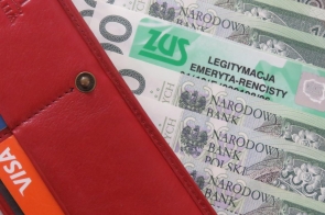Czerwony skórzany portfel z widocznymi kartami płatniczymi w kieszonkach. Obok portfela leżą polskie banknoty oraz zielona legitymacja ZUS z napisem „Legitymacja emeryta-rencisty”.