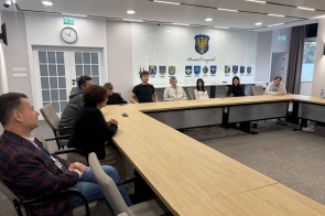 Grupa młodzieży i dorosłych siedzących przy dużym stole konferencyjnym, w jasnej sali.