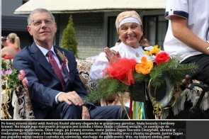  Wójt Andrzej Kozieł w granatowym garniturze i Janina Żagan w ludowym stroju siedzą na udekorowanym wozie, uczestnicząc w dożynkowym korowodzie. 