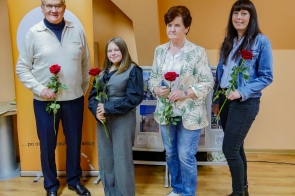 Laureaci konkursu „Selfie z marką Śląsk Cieszyński” stoją obok siebie z czerwonymi różami w dłoniach. Uśmiechnięci pozują do pamiątkowego zdjęcia na tle pomarańczowego baneru wydarzenia, symbolicznie zamykając jubileuszową edycję konkursu.
