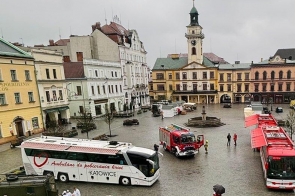 Rynek w Cieszynie, na którym stoją pojazdy, w tym ambulans do poboru krwi i wozy strażackie, a ludzie poruszają się po mokrej nawierzchni w deszczowy dzień.