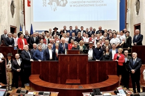 Duża grupa osób ustawiona do wspólnego zdjęcia w sali obrad, część uczestników w strojach ludowych, w tle ekran z napisem o Roku Górali.