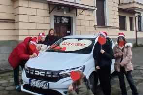 Dyrektor placowki wraz z wychowankami na tle otrzymanego białego samochodu.