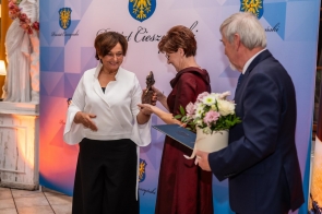 Starosta Cieszyński Janina Żagań, wręcza nagrodę Lidii Lankocz w towarzystwie Stanisława Kubiciusa Przewodniczącego Rady Powiatu, który trzyma bukiet kwiatów i teczkę. W tle ścianka Powiatu Cieszyńskiego.