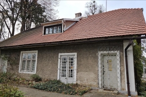 Domek Ogrodnika – Muzeum Zofii Kossak-Szatkowskiej w Górkach Wielkich od strony dawnego parku dworskiego, niewielki historyczny budynek z jasną elewacją i spadzistym, ceglanym dachem, otoczony zielenią.