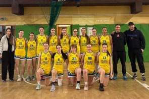 Grupa zawodniczek w żółtych strojach koszykarskich oraz trener na sali gimnastycznej pod koszem do gry.