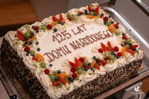 Tort z okazji 125 lecia Domu Narodowego w Cieszynie. Tort prostokątny z kremem, udekorowany owocami i napisem „100 LAT Domu Narodowego”. Na wierzchu widoczne świeczki. 