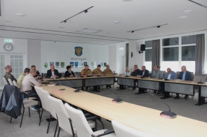 W sali konferencyjnej Starostwa w Cieszynie przy długim stole obradują przedstawiciele służb mundurowych, instytucji i samorządu, skupieni na dyskusji. W tle herb powiatu i godła gmin.