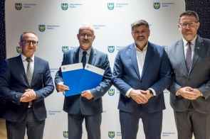 Czterech mężczyzn w garniturach pozuje do zdjęcia na tle ścianki z logotypami Województwa Śląskiego.