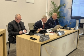 Prezydium Rady Powiatu Grzegorz Konieczny, Stanisław Kubicius, Jarosław Bodak. Na blacie znajdują się dokumenty, tablety, mikrofony i tabliczki imienne, a w tle widać ekran oraz elementy z herbem Powiatu Cieszyńskiego.