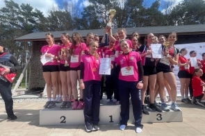 Grupa dziewcząt w różowych koszulkach stoją na podium z pucharami, medalami i dyplomami.