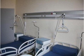 W pomieszczeniu znajdują się dwa łóżka szpitalne z niebieskimi materacami. Nad nimi zamontowane są uchwyty i wysięgniki do podciągania się oraz panel z instalacjami medycznymi. Między łóżkami stoi mała szafka.