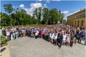 Uczestnicy wydarzenia pozują do wspólnego zdjęcia na dziedzińcu przed budynkiem. Na fotografii widoczna jest liczna grupa osób zgromadzonych na otwartej przestrzeni. W tle znajdują się drzewa, park oraz zabudowania.