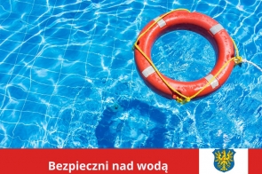 Jasnoniebieska woda basenu z delikatnymi refleksami słońca, po której unosi się pomarańczowe koło ratunkowe z białymi odblaskami i żółtą liną. W dolnej części grafiki czerwony pasek z napisem „Bezpieczni nad wodą” oraz herbem i logotypem Powiatu Cieszyńskiego.