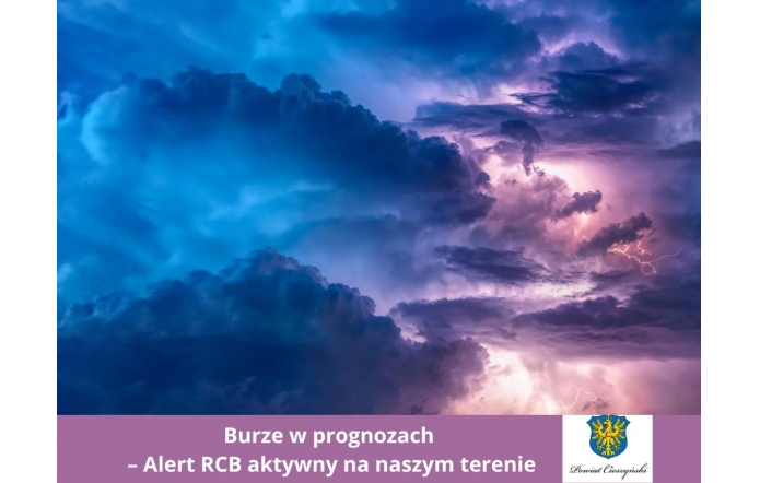Ciemne, gęste chmury burzowe rozświetlają błyskawice w odcieniach fioletu i niebieskiego. U dołu umieszczono pasek w kolorze fioletowym z informacją o aktywnym alercie RCB i herbem Powiatu Cieszyńskiego.