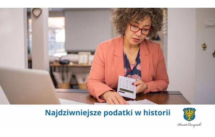 Kobieta w okularach i eleganckim stroju siedzi przy biurku, trzymając kalkulator i przeglądając dokumenty. Na dole widoczny napis „Najdziwniejsze podatki w historii” oraz herb Powiatu Cieszyńskiego.