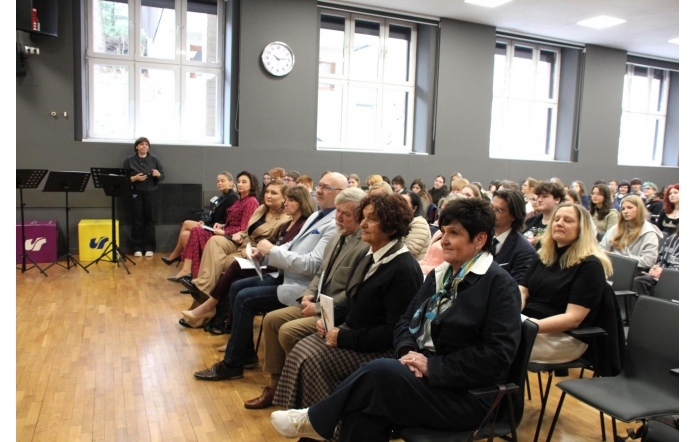 Zaproszeni goście oraz uczniowie siedzą na krzesłach w sali konferencyjnej. Goście ubrani w eleganckie stroje.
