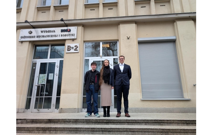 Troje młodych laureatów pozuje przed wejściem do Wydziału Inżynierii Mechanicznej i Robotyki. Eleganckie stroje, uśmiechy i duma w oczach podkreślają rangę wydarzenia, w którym właśnie wzięli udział.