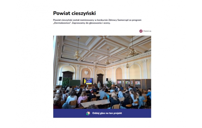 U góry widoczny nagłówek Powiat Cieszyński z informacją o nominacji do konkursu,  poniżej zdjęcie sali wykładowej z wysokim, dekoracyjnym sufitem i żyrandolami, wypełniona siedzącymi uczniami w stronę ekranu z prezentacją. Na dole przycisk "Oddaj głos na ten projekt".
