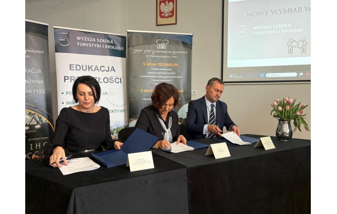 Trzy osoby siedzą przy stole, od lewej: Kornelia Zubek Dyrektor ZSGH w Wiśle,  Janina Żagan Starosta Cieszyński oraz dr hab.Marek Nocoń Dziekan Wydziału Nauk Społecznych, podpisują dokumenty. Za nimi stoją roll-upy z informacjami o szkołach, na ścianie godło Polski i ekran.