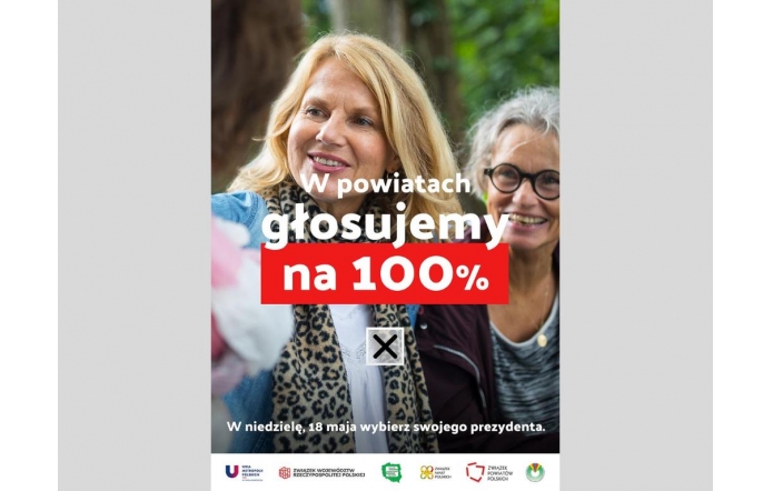 Uśmiechnięte kobiety stoją na tle zieleni. Na środku widnieje tekst: "W powiatach głosujemy na 100%". Na dole napis: "W niedzielę, 18 maja wybierz swojego prezydenta". Znajdują się tam też loga organizacji, w tym Unii Metropolii Polskich.