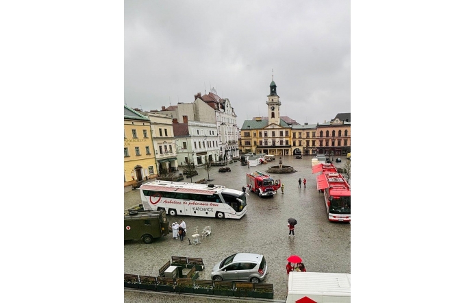 Rynek w Cieszynie, na którym stoją pojazdy, w tym ambulans do poboru krwi i wozy strażackie, a ludzie poruszają się po mokrej nawierzchni w deszczowy dzień.