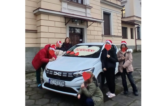 Dyrektor placowki wraz z wychowankami na tle otrzymanego białego samochodu.
