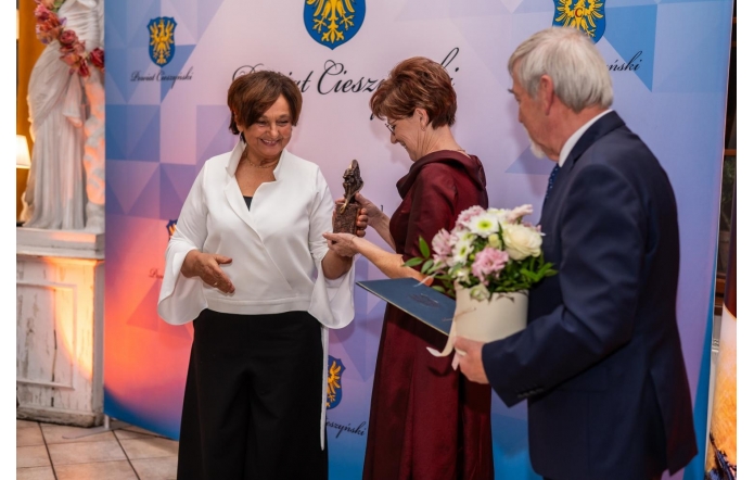 Starosta Cieszyński Janina Żagań, wręcza nagrodę Lidii Lankocz w towarzystwie Stanisława Kubiciusa Przewodniczącego Rady Powiatu, który trzyma bukiet kwiatów i teczkę. W tle ścianka Powiatu Cieszyńskiego.