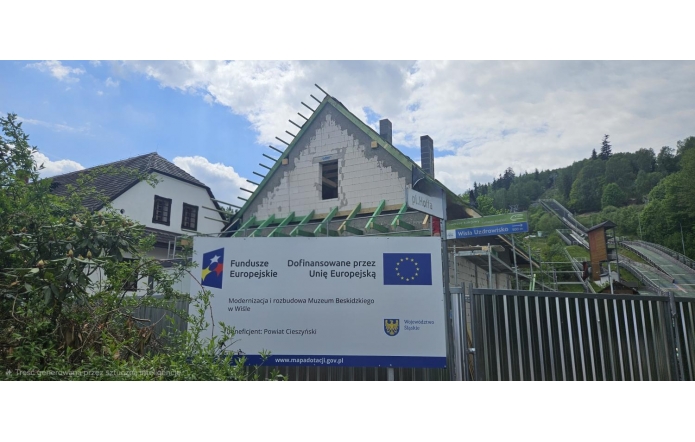 Tablica informacyjna projektu współfinansowanego ze środków Unii Europejskiej zamontowana na ścianie budynku. Widoczne są logotypy programu Fundusze Europejskie, Rzeczypospolitej Polskiej, Unii Europejskiej oraz Województwa Śląskiego wraz z informacjami o realizowanym projekcie.