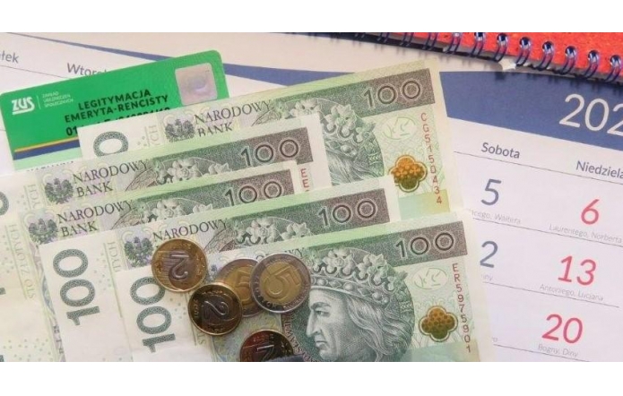 Banknoty stuzłotowe i monety leżą obok zielonej legitymacji emeryta-rencisty ZUS oraz fragmentu kalendarza z listopadowymi datami.